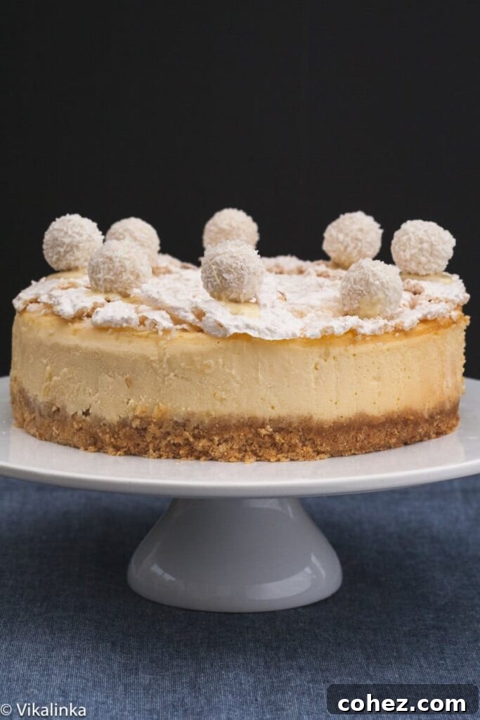 A beautifully presented Raffaello Cheesecake on a white cake stand, showcasing its elegant white topping and smooth sides.