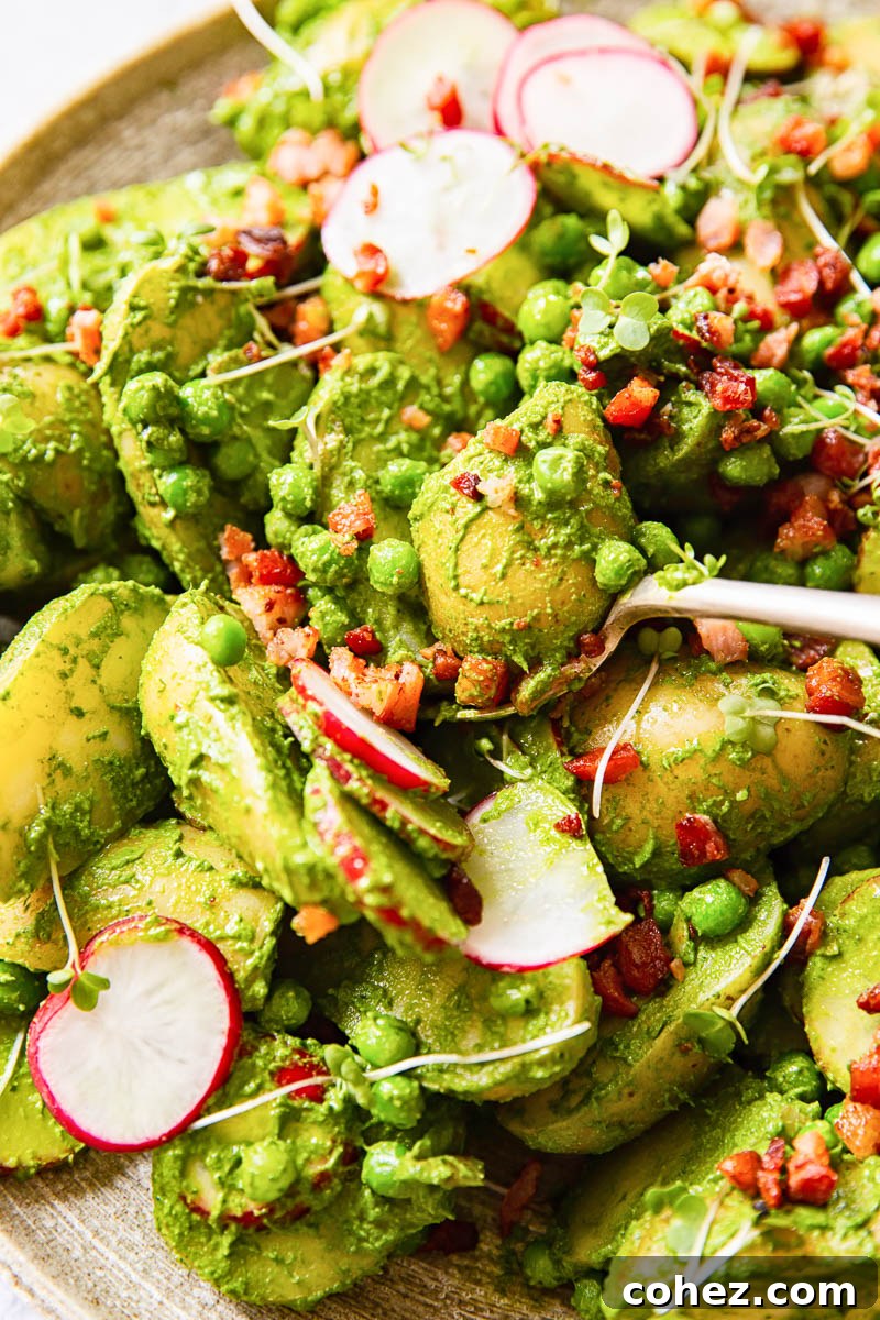 A generously portioned bowl of pesto potato salad, adorned with thinly sliced radishes, bright green peas, and savory bacon pieces, ready to be served.