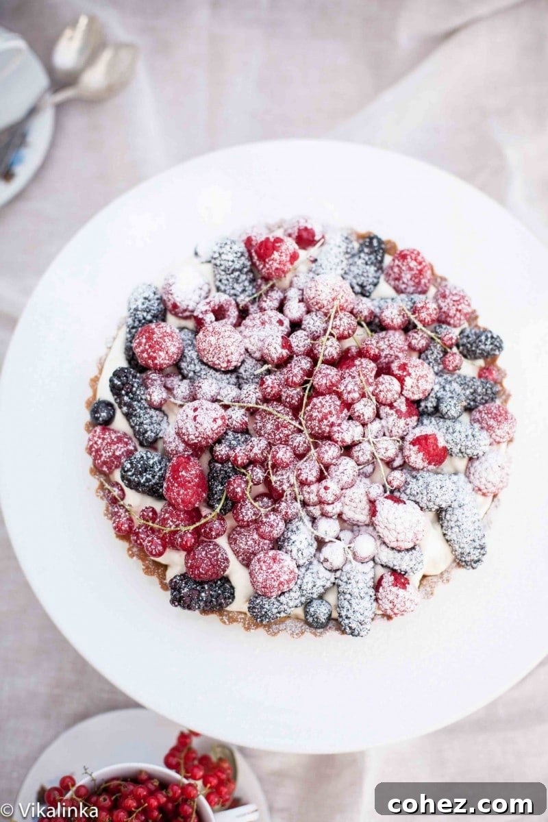 Sweet Summer Berry Bliss 2 Top down view of a vibrant summer berry tart on a white platter, showcasing an assortment of fresh berries, whipped cream, and meringue pieces.