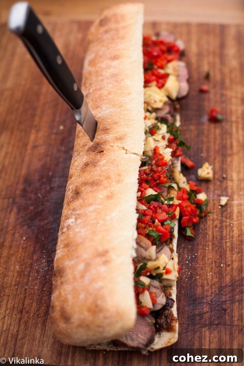 Top-down view of an open ciabatta loaf generously topped with seared duck breast, chopped artichokes, and roasted red peppers.