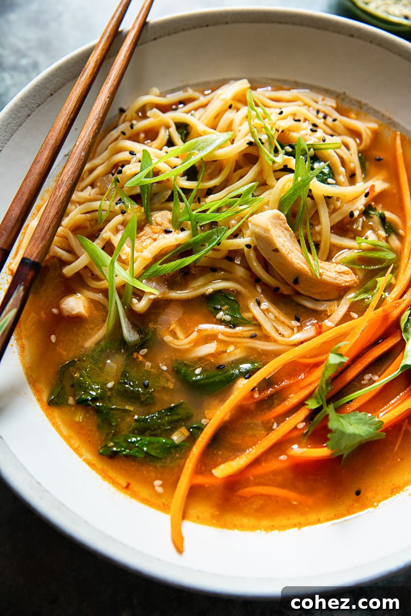 close up image of noodles in broth with chicken, carrots and green onions