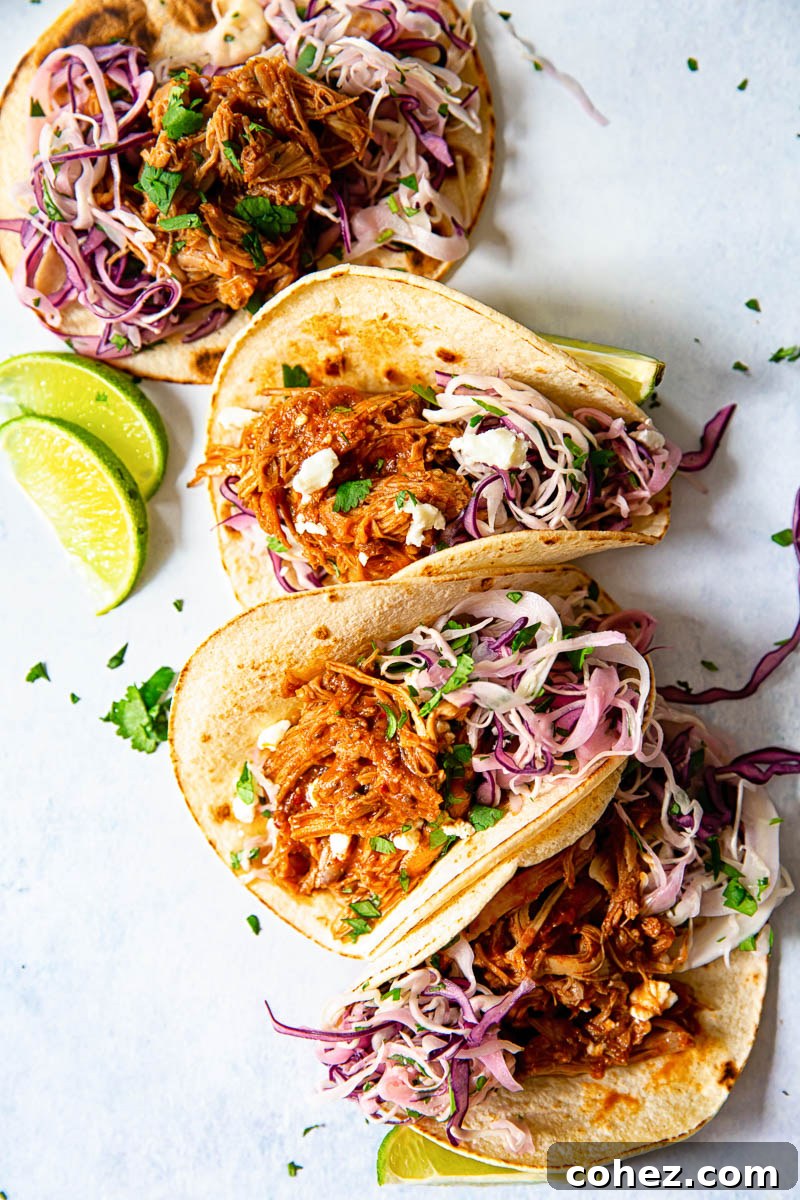 Four soft tacos filled with pulled pork and red and white slaw, garnished with cilantro