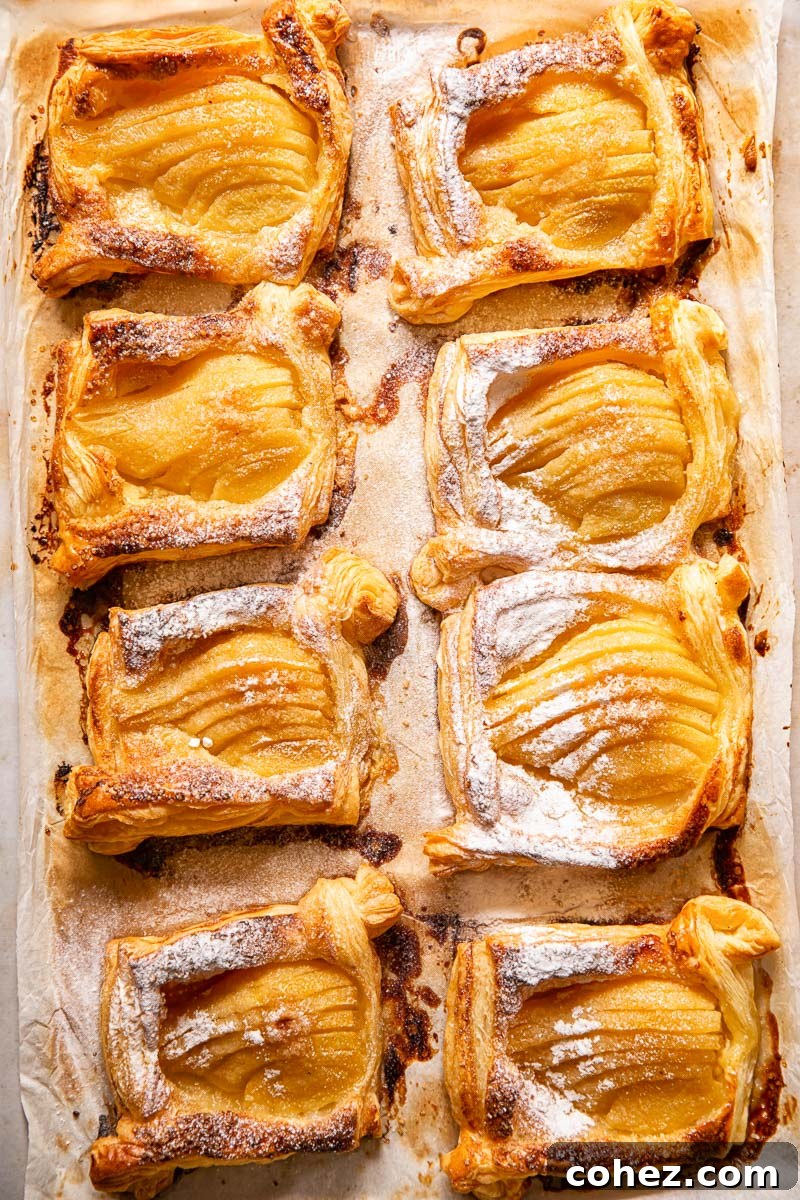 Multiple pear tarts dusted with powdered sugar on a baking sheet