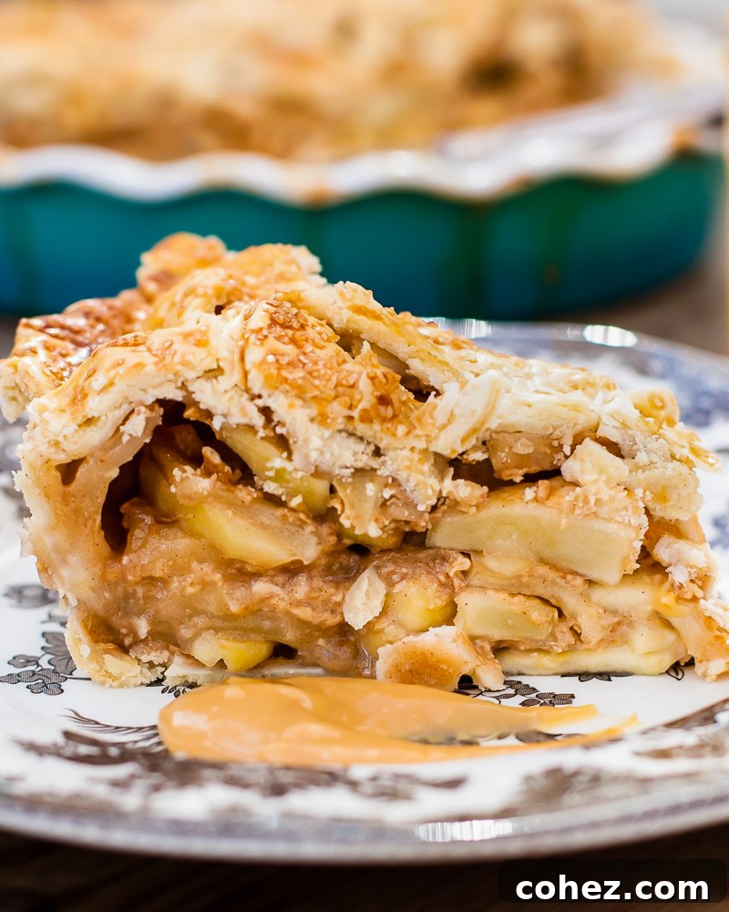 A perfectly baked slice of Dulce de Leche Apple Pie on a white plate, revealing layers of flaky crust and caramelized apple filling.