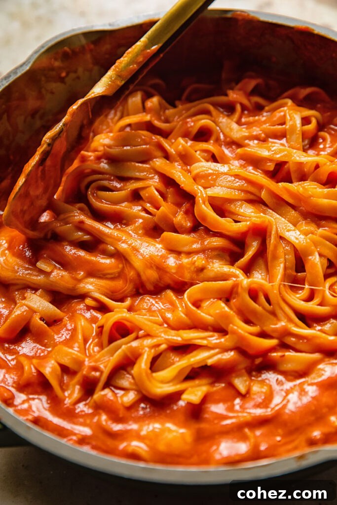 pan with tagliatelle in a red sauce stirred by tongs