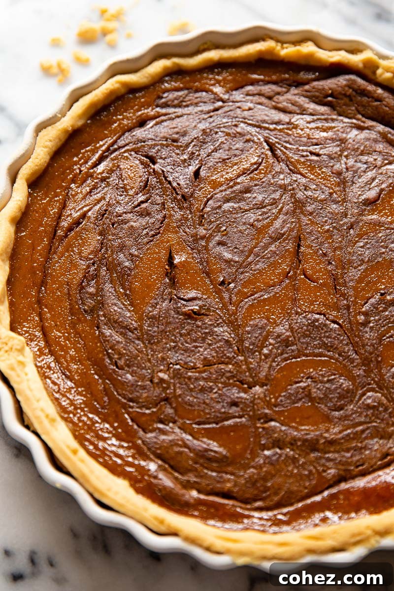 A whole pumpkin pie with a visible chocolate swirl, ready to be sliced, sitting on a cooling rack.