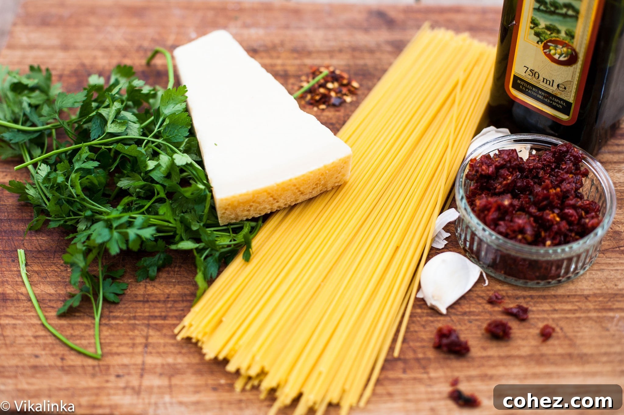 Authentic Spaghetti alla Siciliana Video Recipe 4 A collection of ingredients laid out on a wooden surface: spaghetti, sun-dried tomatoes, garlic, chili flakes, and olive oil.