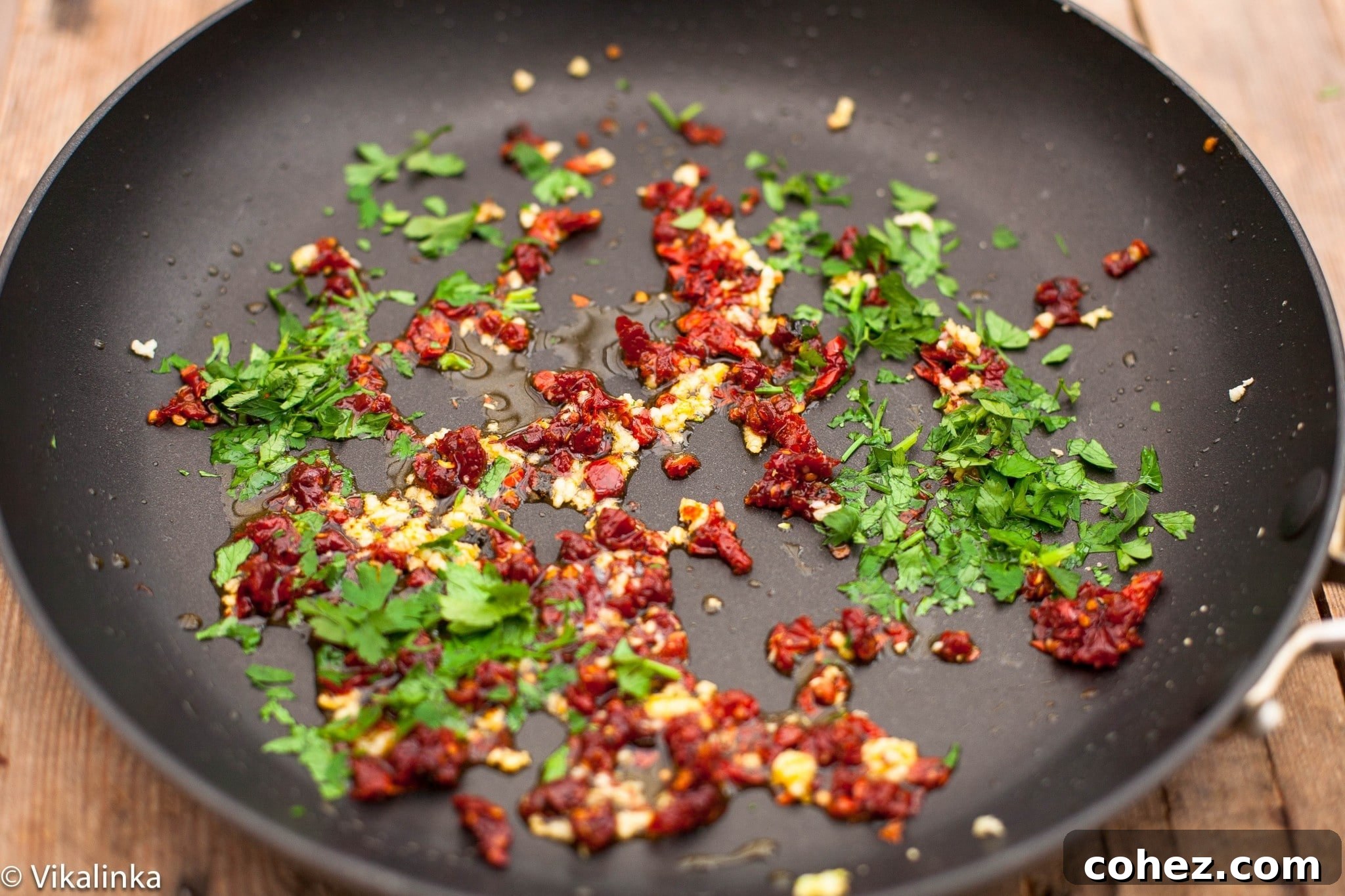 Authentic Spaghetti alla Siciliana Video Recipe 5 Minced garlic, chopped sun-dried tomatoes, and red chili flakes being gently sautéed in olive oil in a pan.