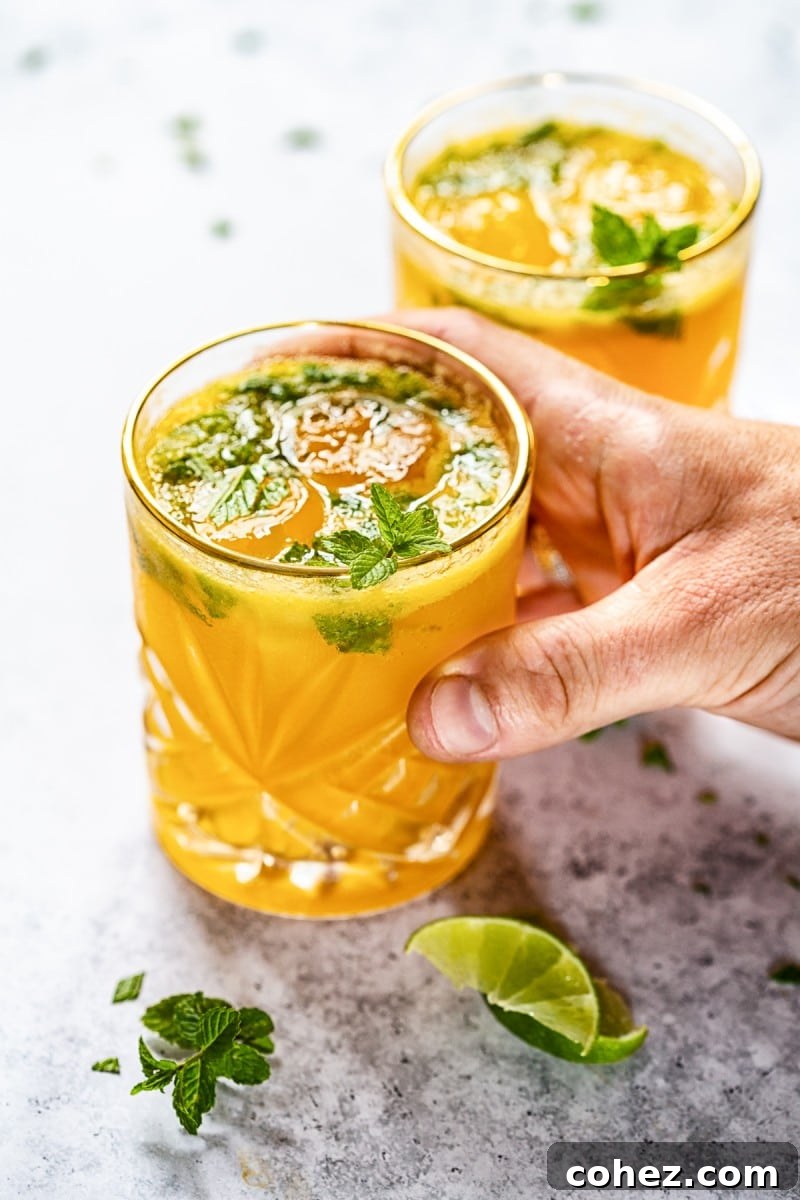 A hand holding a tall glass of mango mojito, with a straw and lime wedges. #mangomojito #cocktailhour
