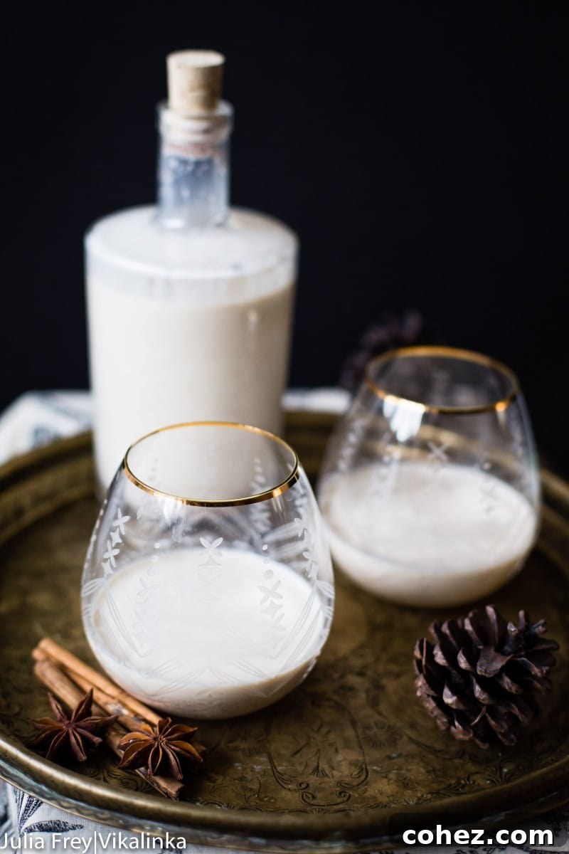 A festive glass of homemade eggnog garnished with a cinnamon stick and fresh nutmeg, presented on a wooden board with pinecones.