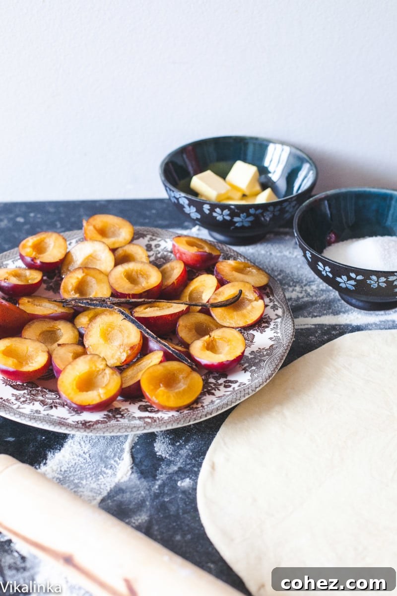 halved plums on a plate, rolled out puff pastry, and a bowl with sugar and butter cubes