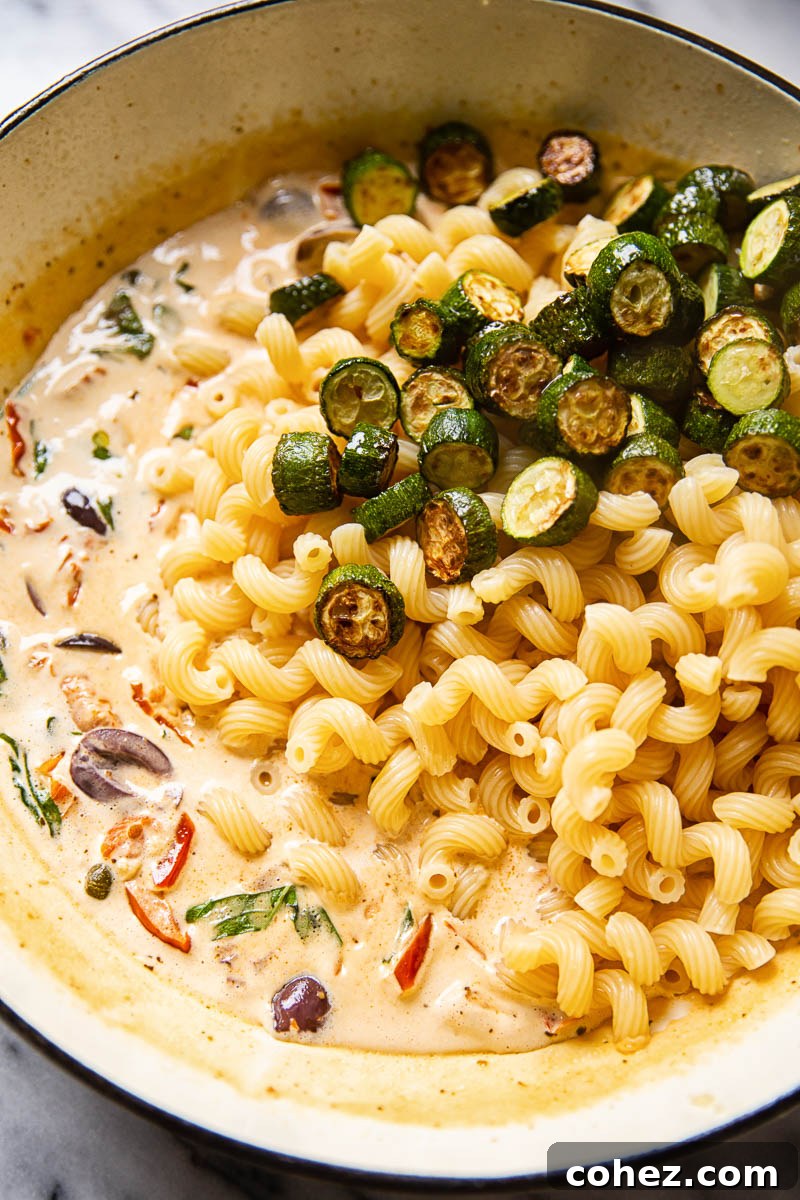 Pan with the Mediterranean pasta ingredients added but not yet mixed together, showcasing vibrant colors.