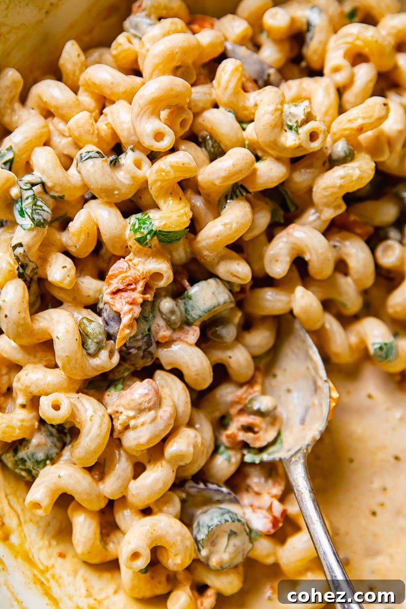 Close up of Mediterranean pasta with zucchini, creamy sauce, and fresh basil, with a serving spoon ready.