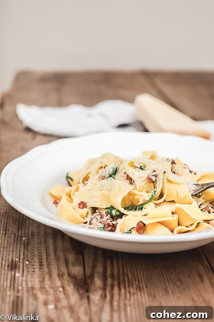 side shot of Pappardelle Carbonara with Arugula on white plate, garnished with parmesan