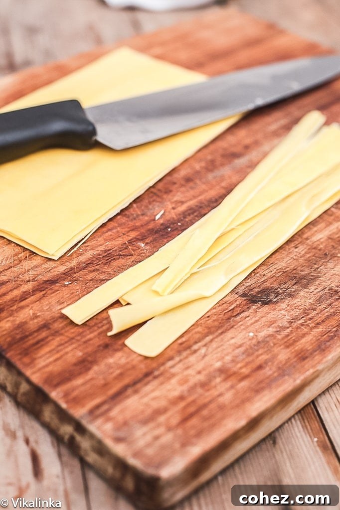 close up of pasta sheets being cut into pappardelle strips on a wooden board