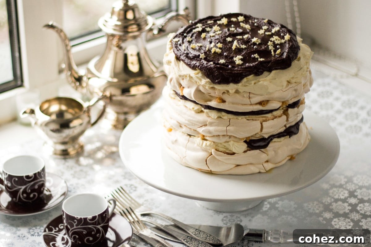 Top down view of an elegantly plated Meringue Mascarpone Cake on a pristine white cake stand, garnished with vibrant fresh berries and a dusting of icing sugar.