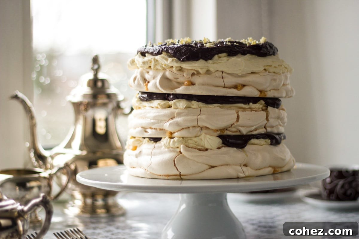 Side view of a beautifully assembled Meringue Mascarpone Cake on an elegant cake stand, with a charming teapot and teacups blurred in the background, suggesting a cozy tea time setting.