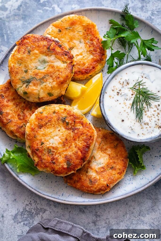 Top down shot of salmon cakes on a plate with a bowl of chive and garlic sauce