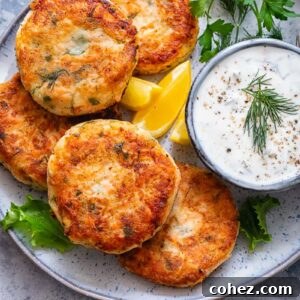 Top down shot of salmon cakes on a plate with a bowl of chive and garlic sauce