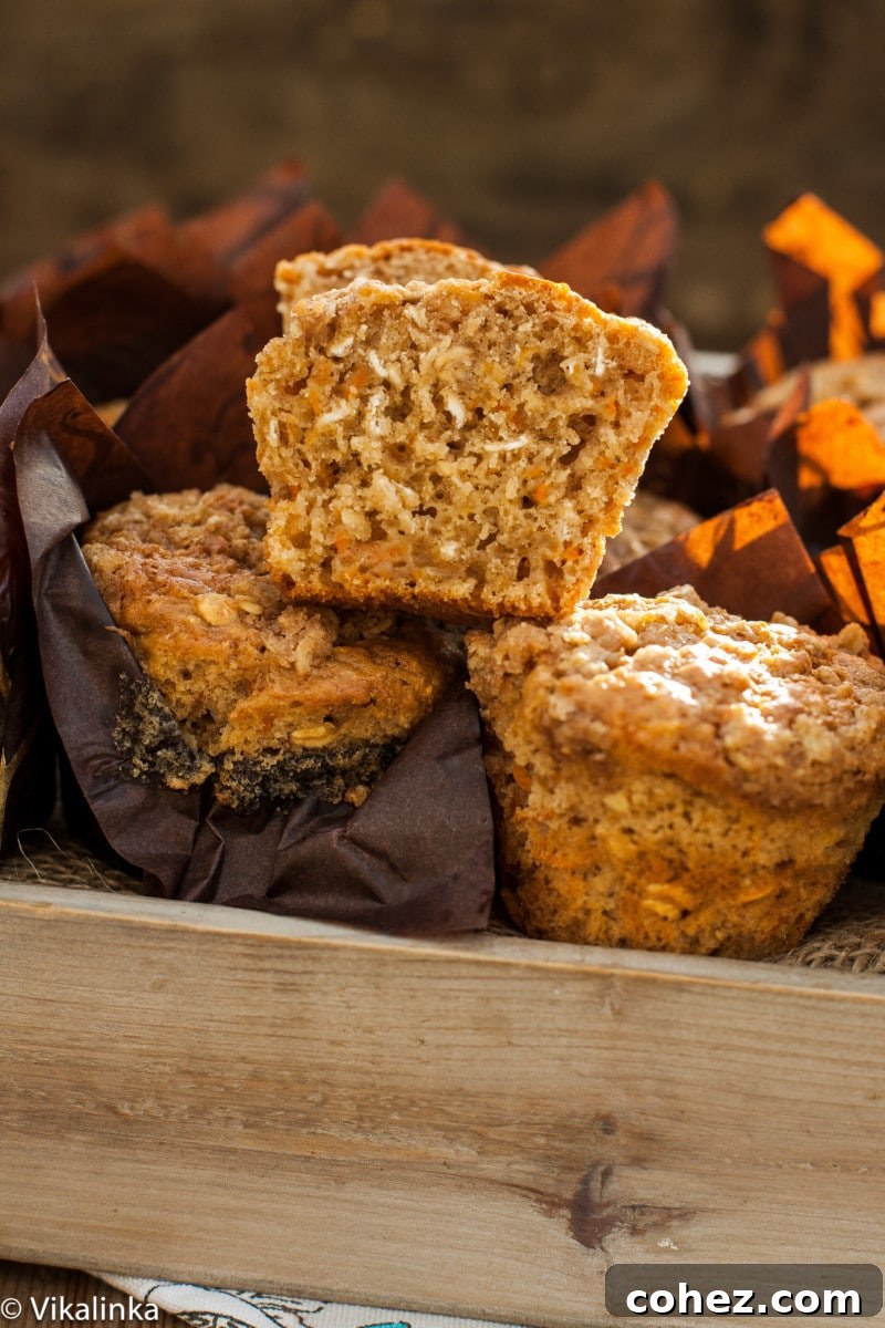 A bread box filled with golden-brown carrot oatmeal muffins, with one muffin elegantly sliced in half to showcase its delightful, moist texture and visible oat flecks.
