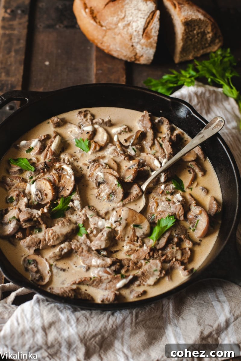 Rich Beef Stroganoff in a black pan on a wooden table, with rye bread in the background.