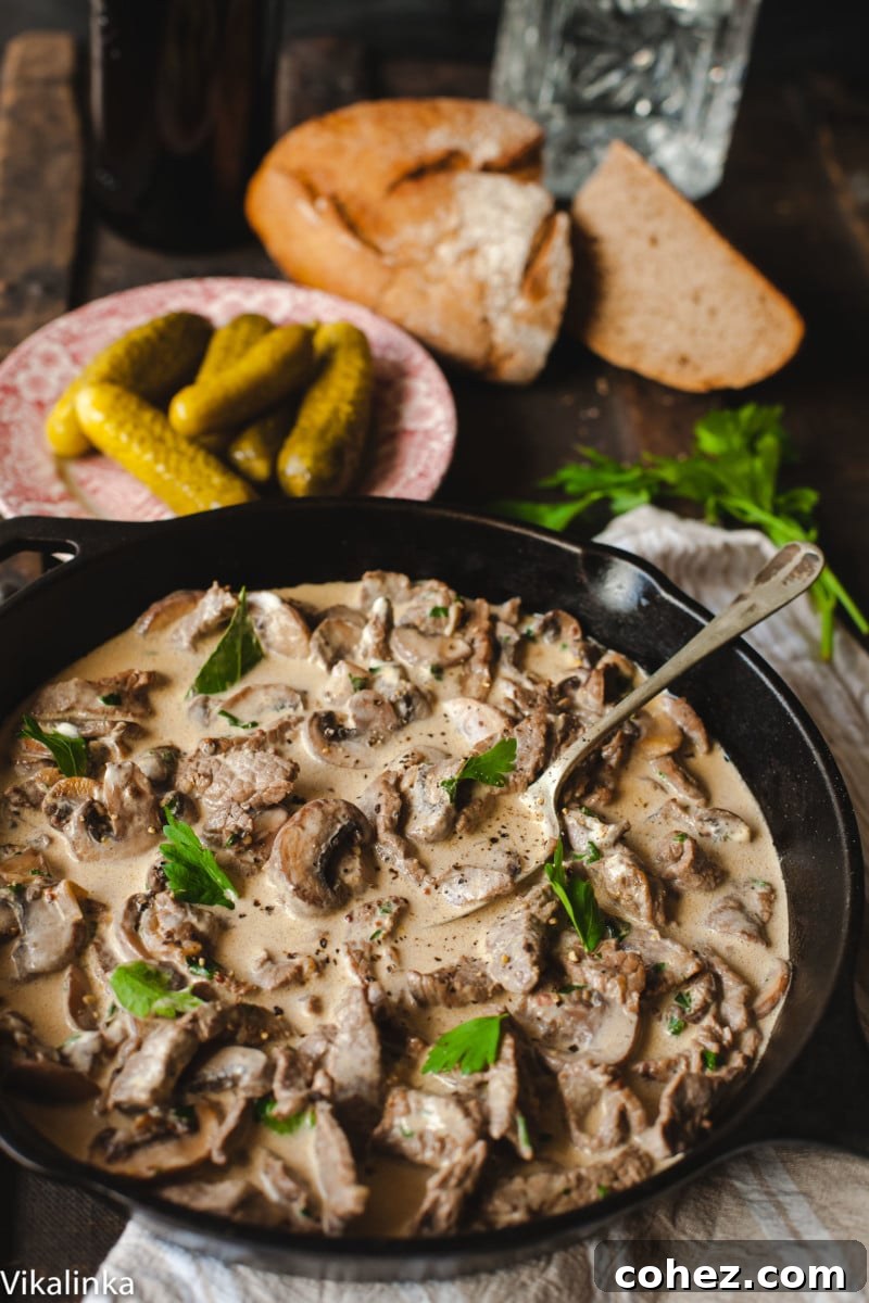 Close-up of creamy meat and mushrooms with sprinkled fresh parsley in a cast iron pan.