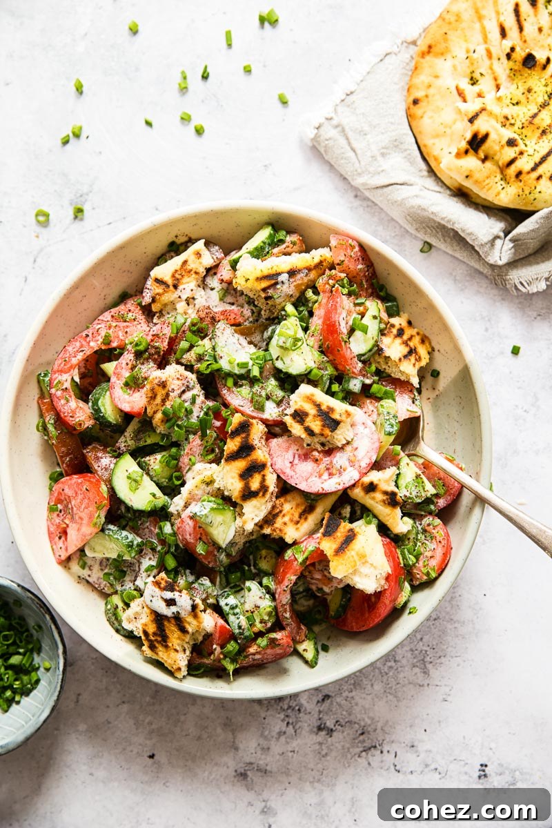 Crisp & Tangy Middle Eastern Fattoush 3 Overhead shot of Fattoush Salad in a cream-colored bowl, garnished with fresh herbs and surrounded by ingredients like sliced green onions and grilled flatbread pieces.