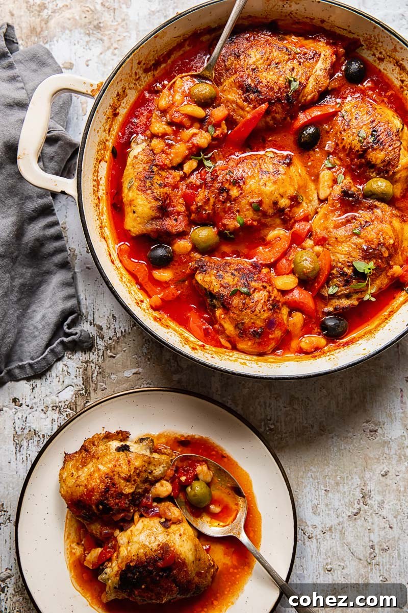 Served Spanish chicken thighs with red peppers and olives in a tomato sauce, with a side of beans and a spoon