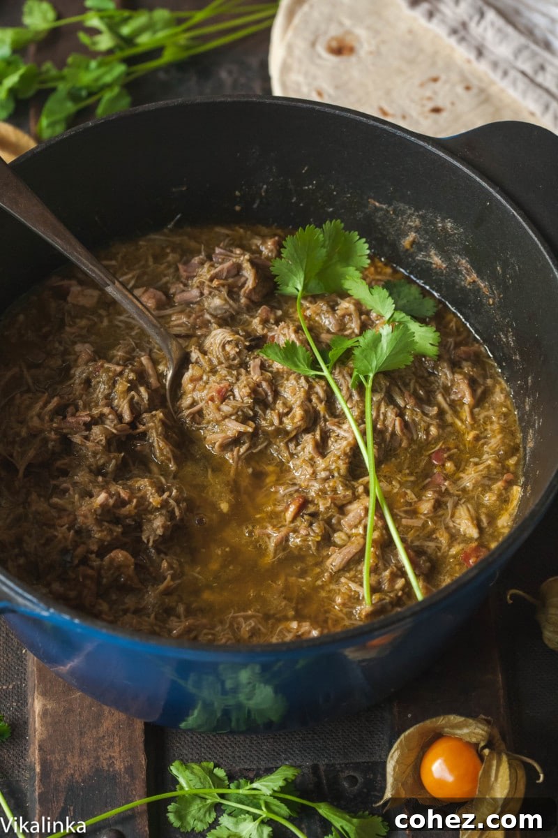 A bubbling pot of Green Chili simmering in a blue Dutch Oven, highlighting its rich texture and color.