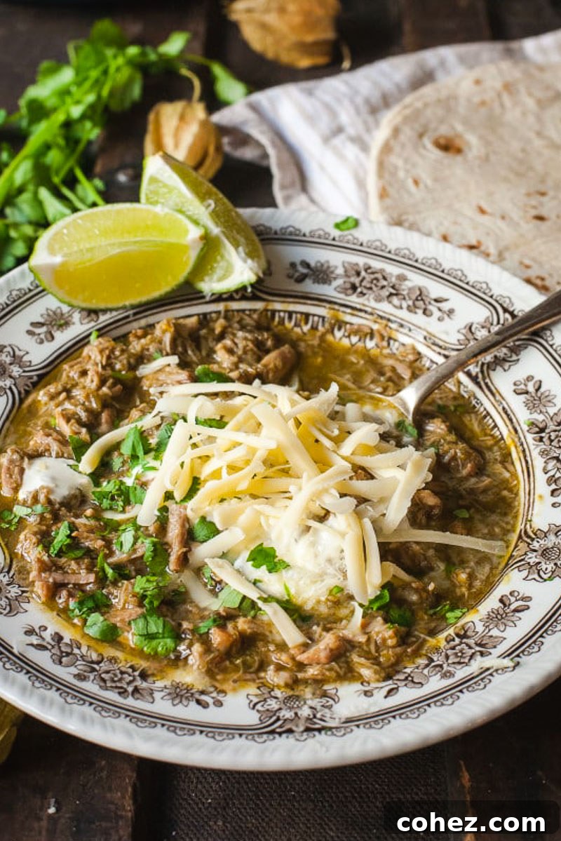 A close-up of Chili Verde served in a bowl, generously topped with grated cheese and fresh chopped cilantro, ready to be enjoyed.