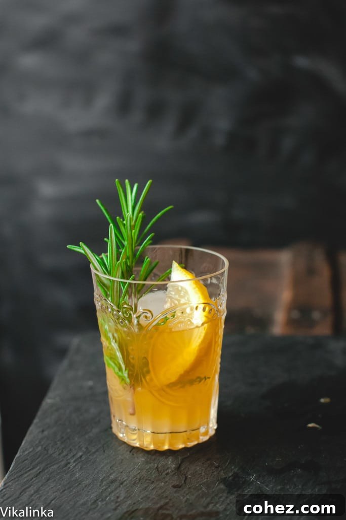 A beautifully garnished Cognac Sour cocktail in a short glass with a lemon slice and rosemary sprig, exuding sophistication and refreshment.