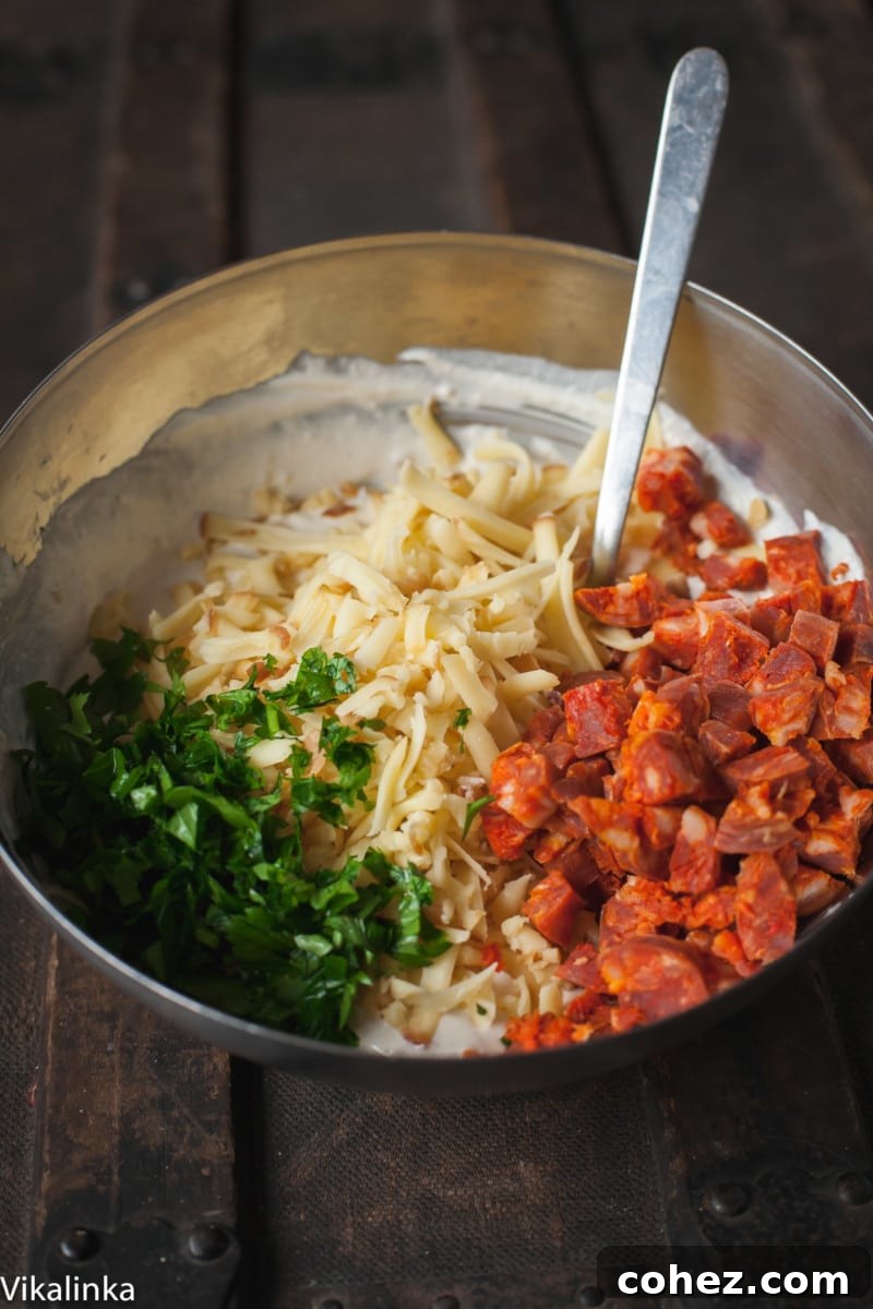 Grated smoked cheese, finely chopped Spanish chorizo, and fresh parsley in a bowl, prepared for the dip.