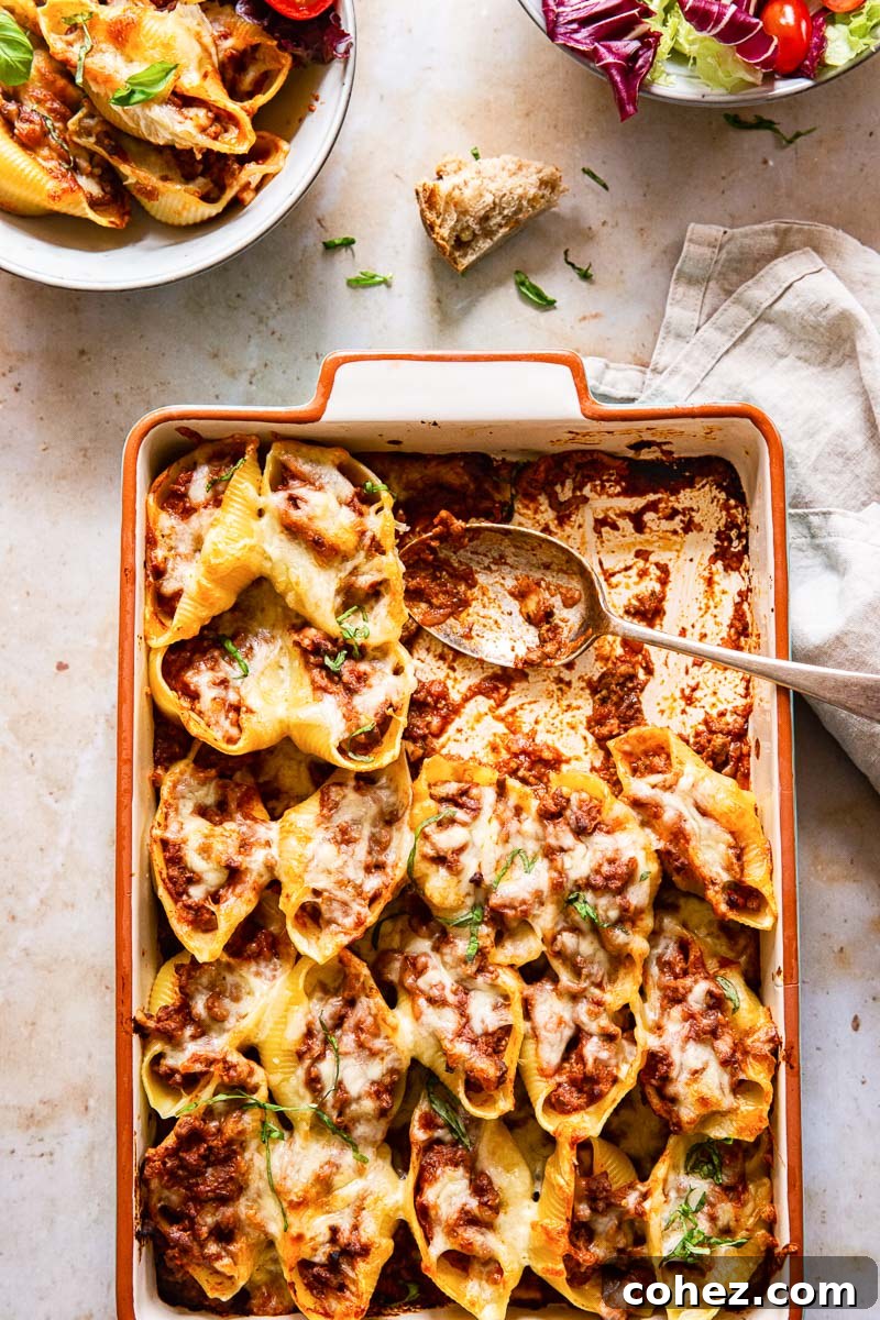Effortless Stuffed Shells with Savory Pesto Beef Ragu 5 Rectangular baking pan with golden-brown baked pasta, served alongside a fresh green salad and an individual bowl of stuffed shells.
