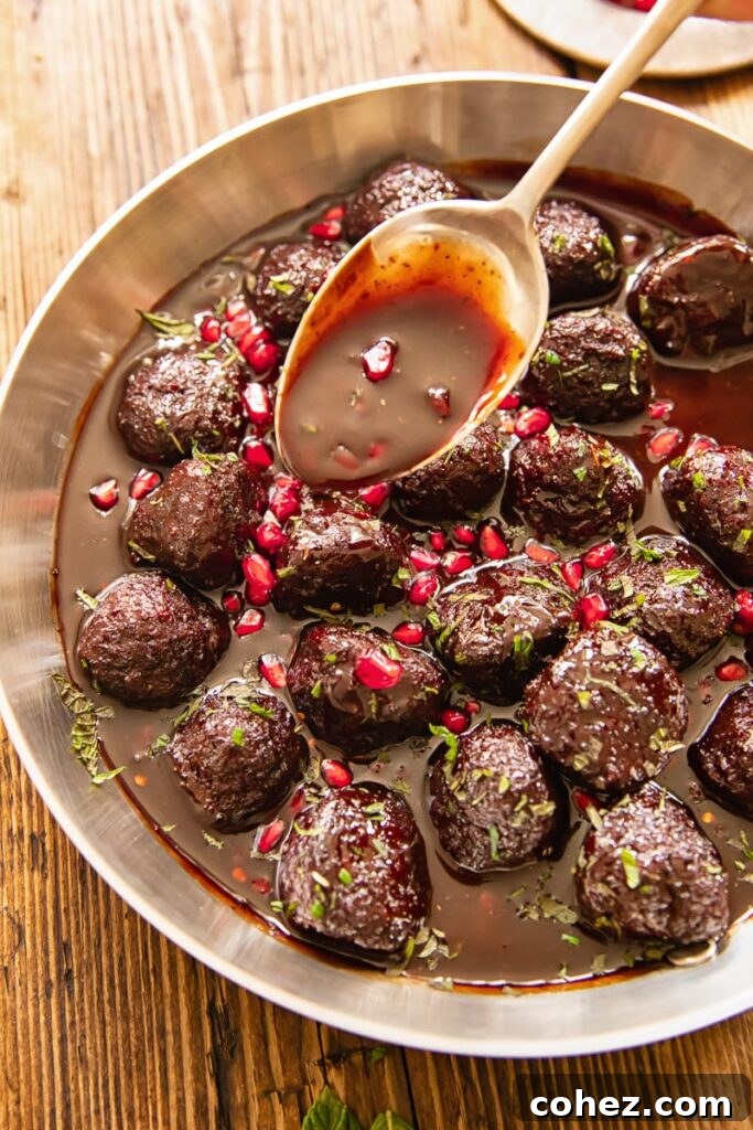 Pomegranate-Glazed Sweet and Sour Meatballs 3 A pan filled with glistening sweet and sour meatballs, with a spoon drizzling more of the rich pomegranate sauce over them.