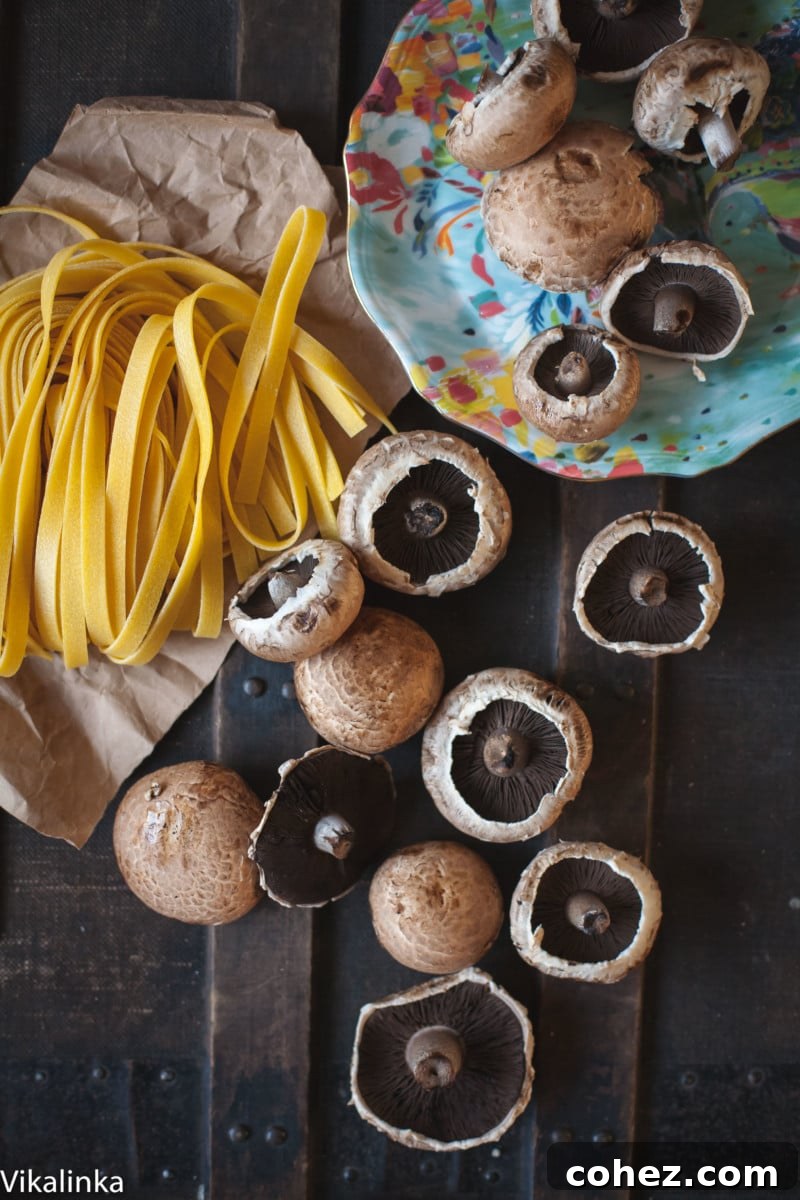 Fresh tagliatelle pasta and sliced Portobello mushrooms arranged artfully on a dark background, highlighting key ingredients.