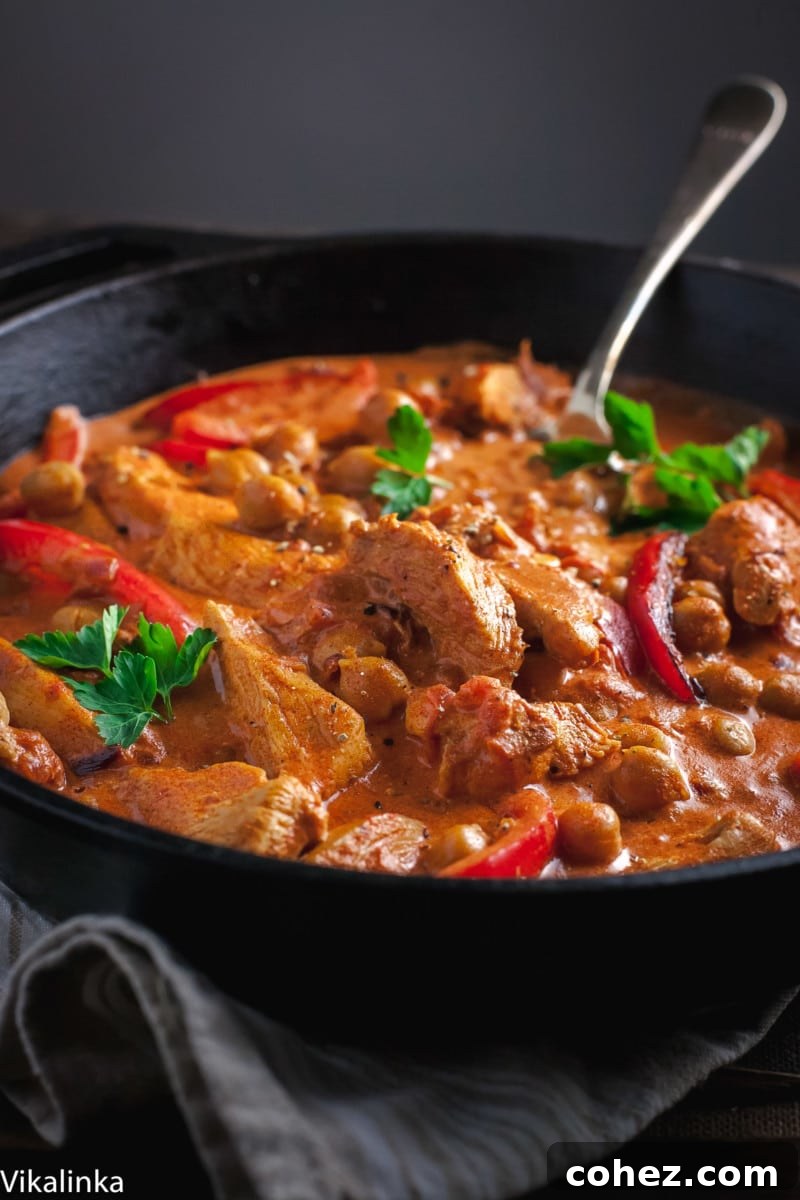 side view of chicken in red sauce with red peppers in cast iron skillet