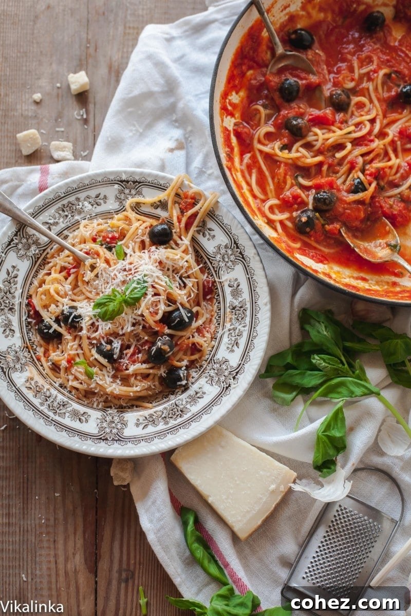 a bowl with spaghetti and black olives, a pan with spaghetti next to it, parmesan cheese and fresh basil. 
