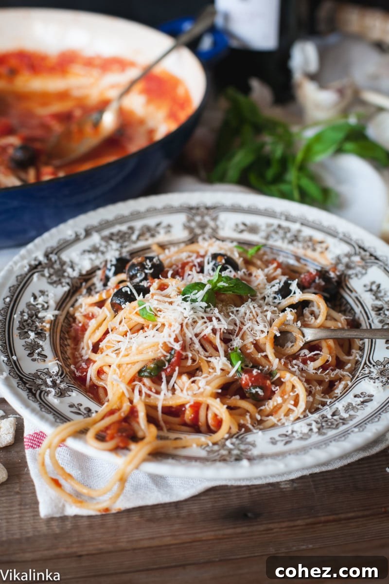 a bowl with spaghetti and black olives topped with parmesan cheese