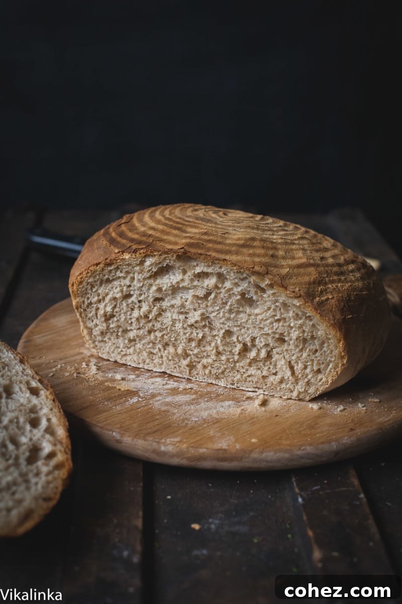 A freshly baked loaf of Rosemary Spelt Bread on a cutting board with a slice removed, showcasing its inviting texture.