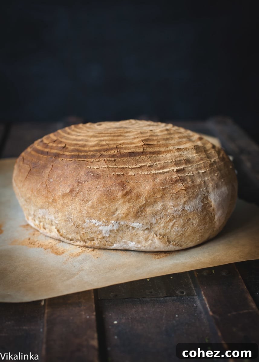 A whole loaf of golden-brown rosemary spelt bread resting on a wooden cutting board, ready to be sliced.