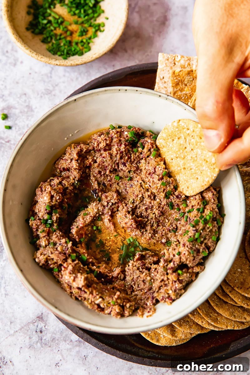 a cracker being dipped into tapenade
