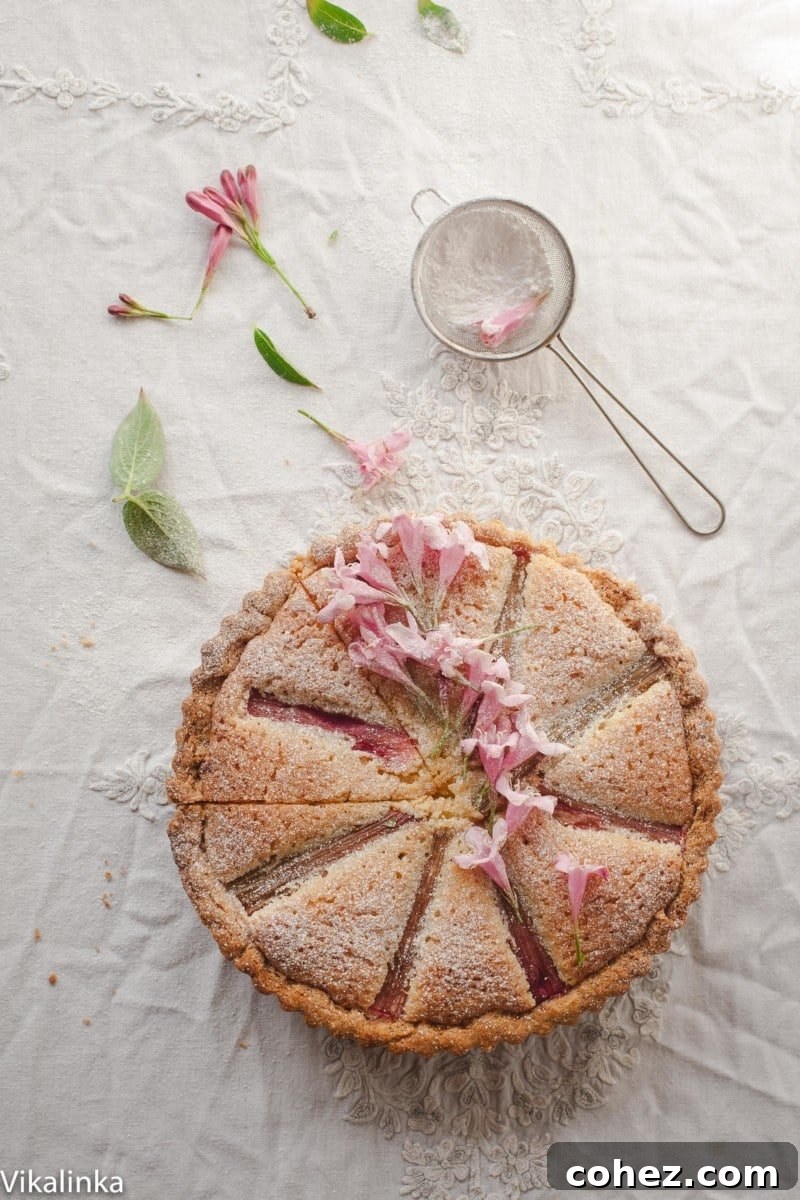 Rhubarb Bakewell Tart decorated with elegant pink flowers, showcasing its beautiful golden-brown top and vibrant fruit filling.