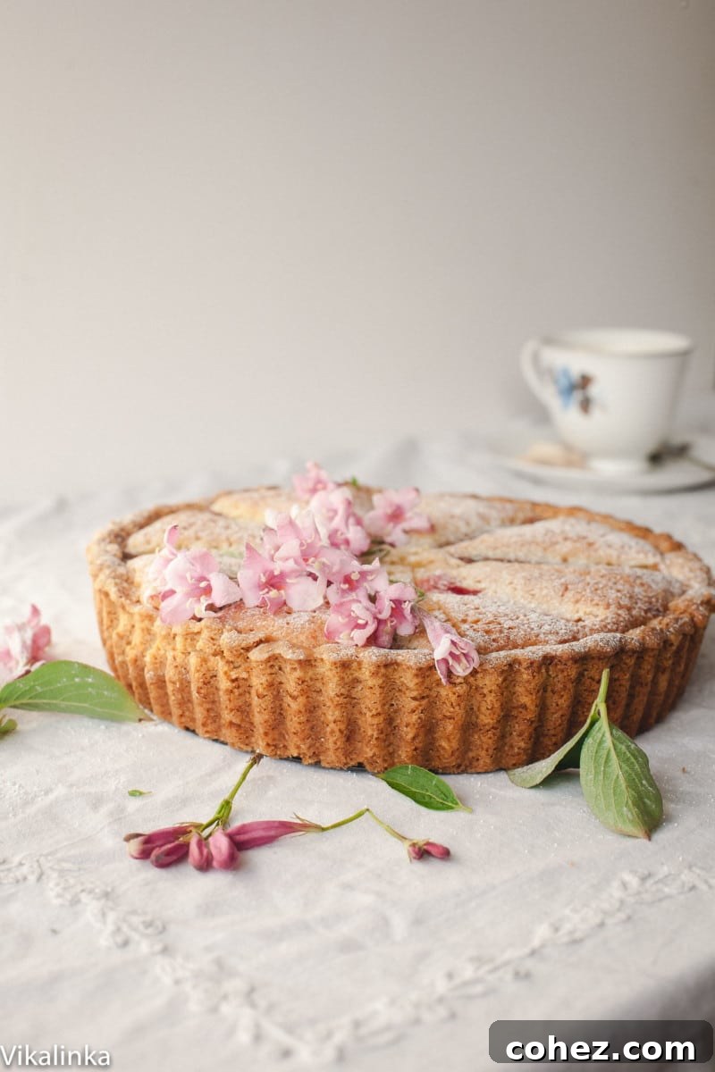 A beautifully presented Bakewell tart, adorned with delicate pink flowers, resting on a white tablecloth, ready to be enjoyed.