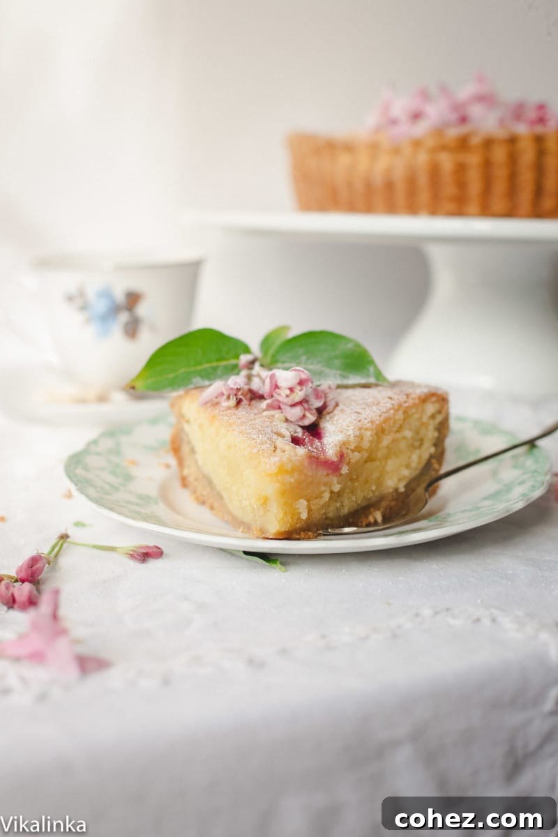 An inviting slice of Rhubarb Bakewell Tart resting on a white plate, revealing its delicious layers of pastry, rhubarb, and frangipane.