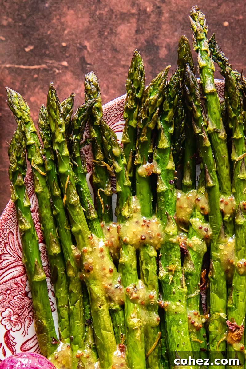 A close-up, top-down view of roasted asparagus with a shimmering mustard vinaigrette dressing, presented on a white serving platter.