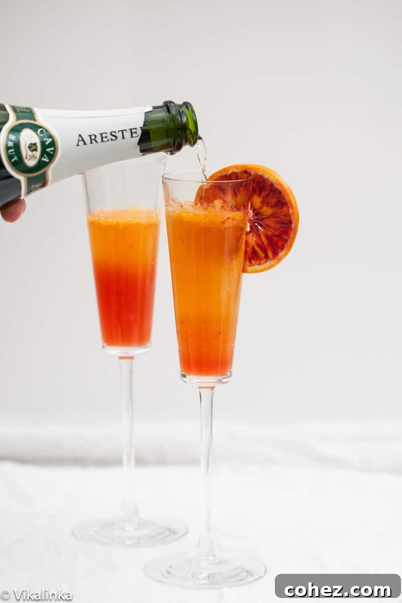 Blood Orange Royale 2 Two French 75 cocktails with blood orange, seen from a high angle, in elegant flutes on a light surface, ready to be enjoyed.