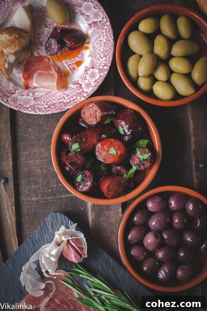 A complete Spanish tapas platter arranged beautifully, featuring the main dish of chorizo in red wine, accompanied by bowls of green olives, mixed cheese, and slices of fresh baguette.