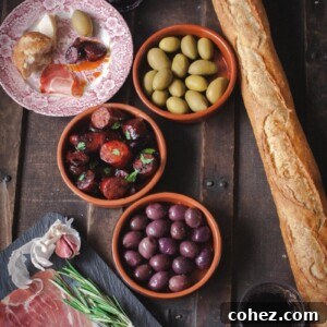 A beautifully presented Spanish tapas spread with crusty baguette slices, olives, and a central dish of sizzling Chorizo in Red Wine in a small pan.