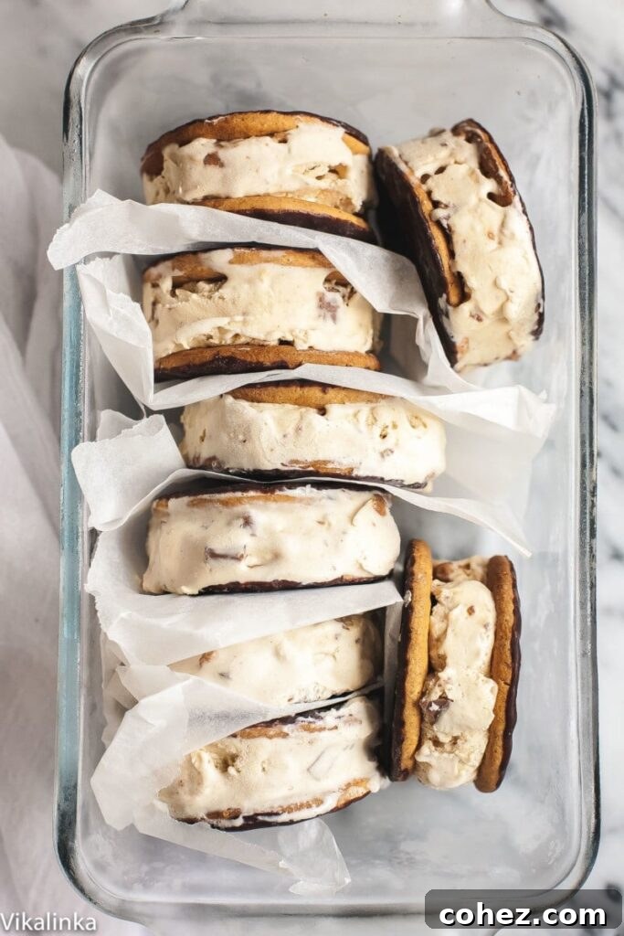 Stacked Cappuccino Daim Ice Cream Sandwiches separated by parchment paper in a clear glass dish, showcasing their inviting layers.