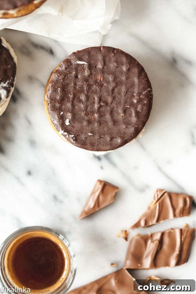 Top-down view of a finished ice cream sandwich, next to scattered chopped Daim bar pieces and a small espresso shot.